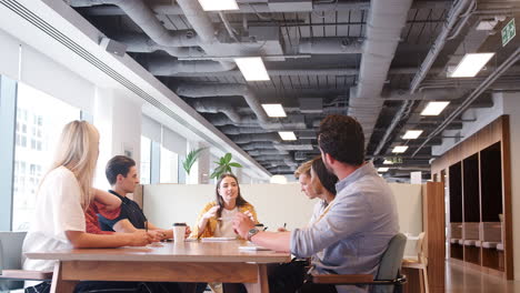 grupo de jóvenes candidatos sentados alrededor de una mesa y colaborando en una tarea en el día de evaluación de contratación de graduados de negocios