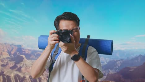 close up of asian male hiker with mountaineering backpack using a camera taking picture while traveling at the top of mountain