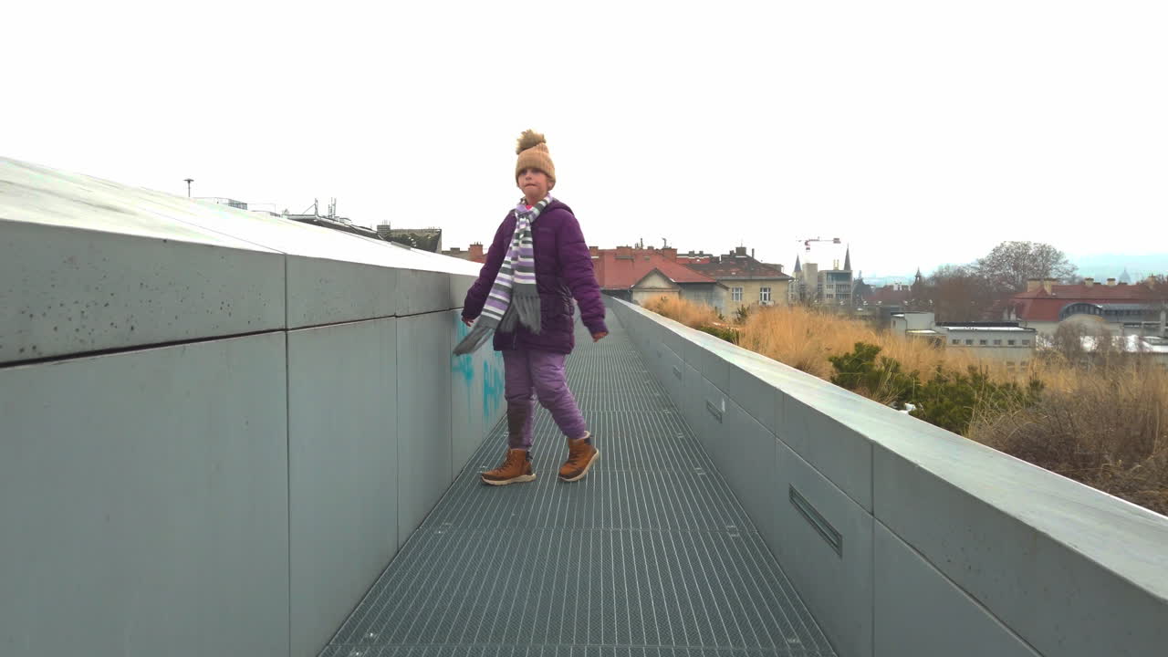 Bakfra, en ung jente går langs en moderne urban sti om vinteren. Kald sesongatmosfære, bybakgrunn og et stille utendørsøyeblikk som fanger barndommens selvstendighet
