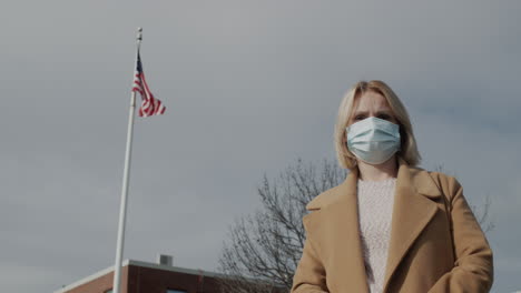 portrait of a woman in a protective mask against the background of a building with an american flag