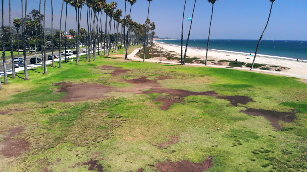 toma aérea volando rápido sobre un piloto de drones masculino hasta las palmeras y el océano pacífico azul en la costa arenosa de santa barbara, california