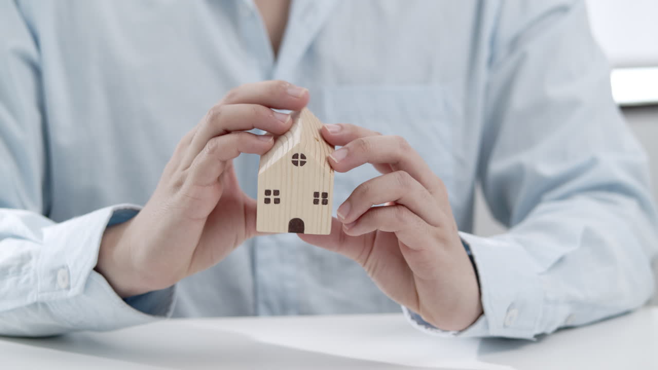 Close-up of a man holding a miniature wooden house as he envisions his real estate opportunities.