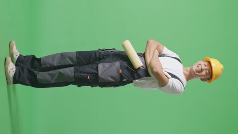 full body side view of asian man painter wearing safety helmet smiling and crossing his arms while standing in the green screen background studio