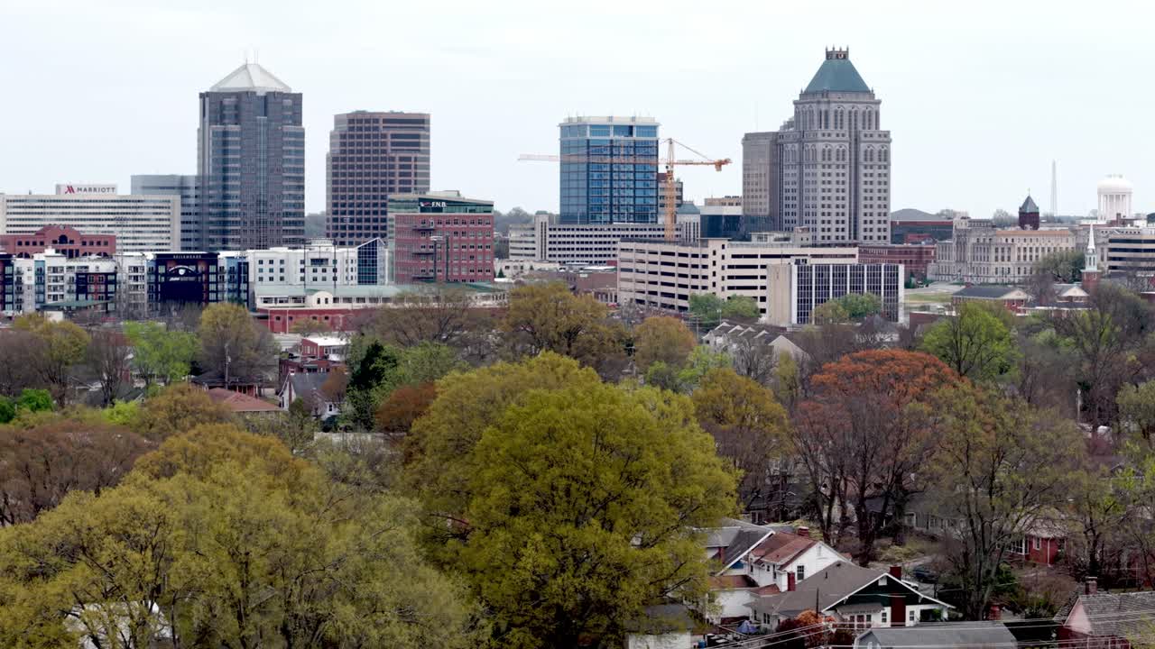 Luftfoto som zoomer inn på Greensboro, North Carolina skyline i tretopphøyde.