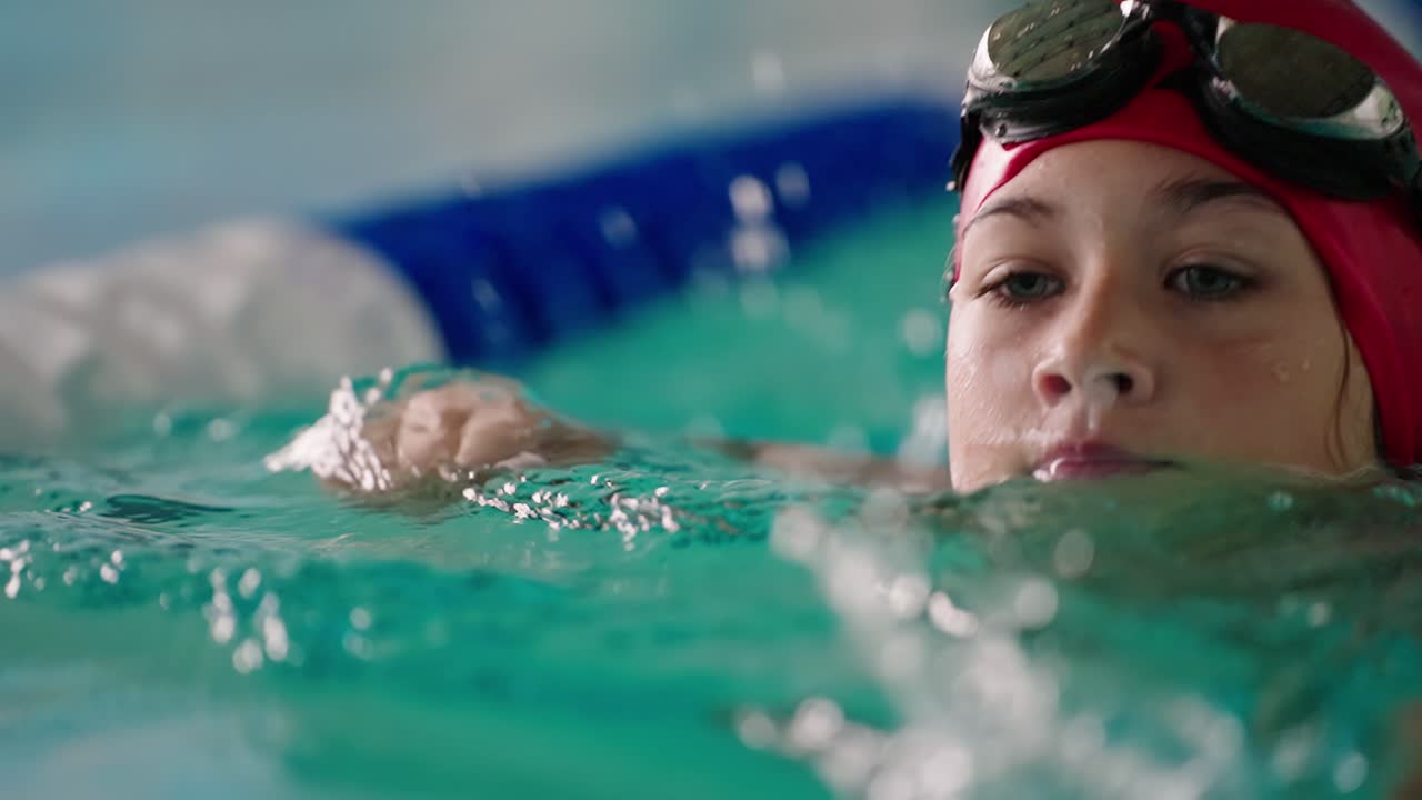 Nahaufnahme einer jungen Schwimmerin im Pool mit roter Badekappe und Schwimmbrille