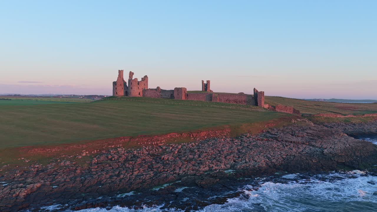 Ruinerne af Dunstanburgh Slot på Northumberland-kysten ved solopgang