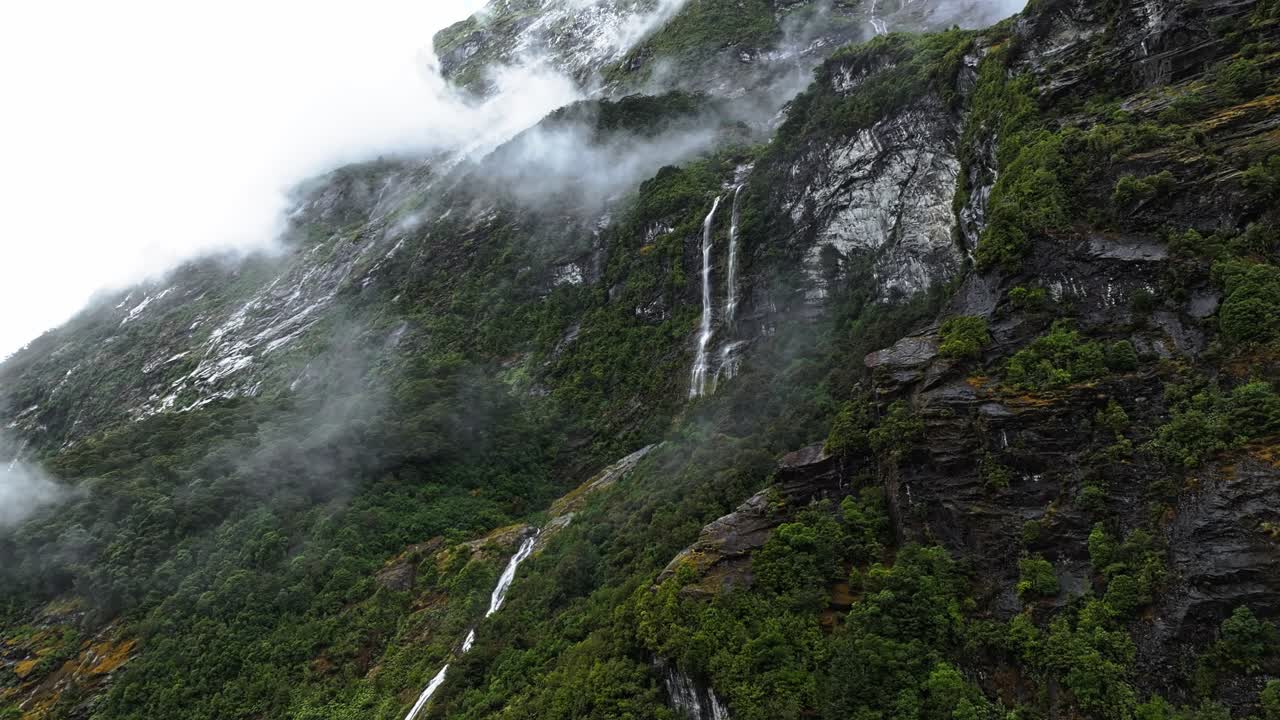 cascadas a lo largo de los bordes de los acantilados de milford sound con nubes bajas sobre el bosque