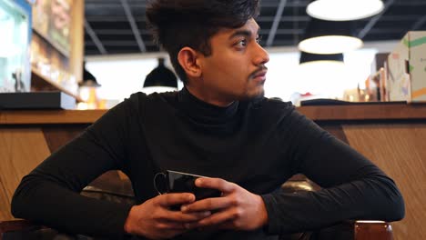 Handsome-Sri-Lankan-man-holding-and-drinking-coffee-while-thinking-in-cafe