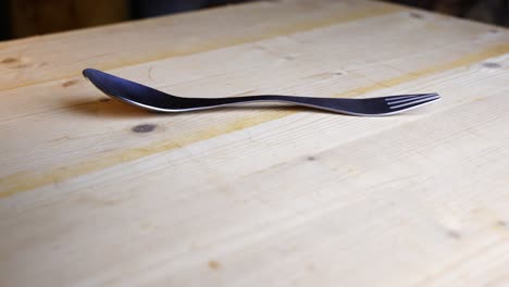 Spork-lies-on-a-wooden-table-and-rotates-against-a-dark-background