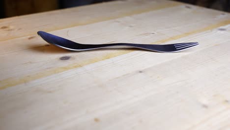 spork lies on a wooden table and rotates against a dark background