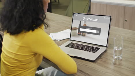 biracial woman at table using laptop, online shopping for beauty products, slow motion