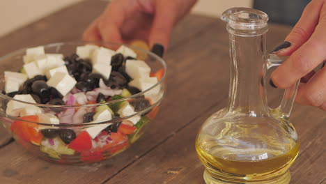 olive oil being poured from bottle over feta salad bowl on kitchen table