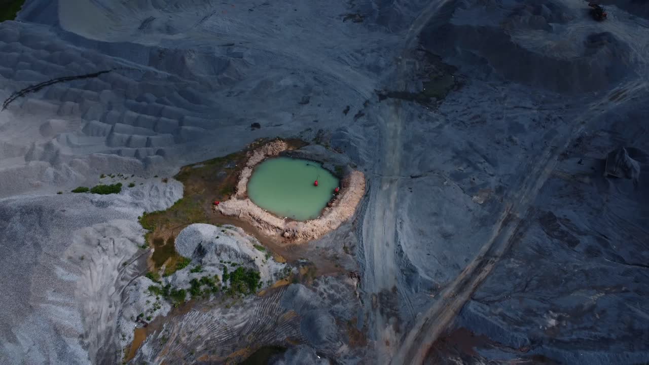 Drone video captures a desolate quarry landscape with a central turquoise pond under dramatic lighting. The scene reveal intricate earthy tones textures and Granite in a barren expanse, Abuja, Nigeria