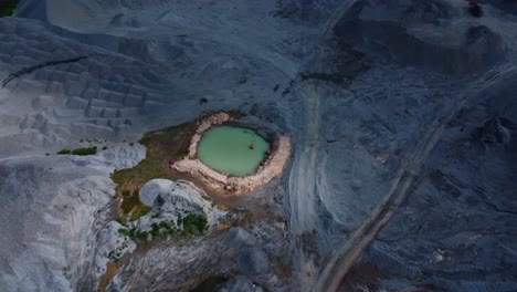 drone video captures a desolate quarry landscape with a central turquoise pond under dramatic lighting. the scene reveal intricate earthy tones textures and granite in a barren expanse, abuja, nigeria