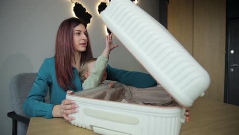 a woman and a baby bond over the contents of a suitcase in a heartwarming video a heartwarming video of a woman affectionately holding a baby at a table opening a suitcase capturing the tender moment as the mother and child bond over its contents