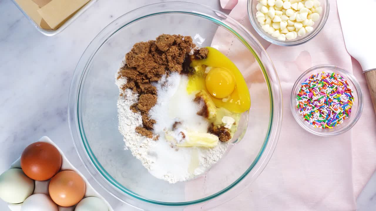 Baking confetti sugar cookies and using a white electric mixer and adding salt to the batter. In the kitchen making a dessert. Making confetti cookies with a white background, pink napkin and eggs