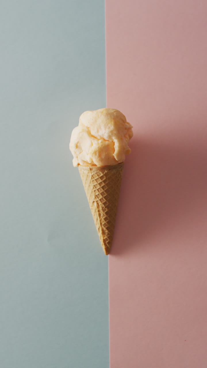 video vertical de cono con helado tendido en superficie gris pastel y rosa