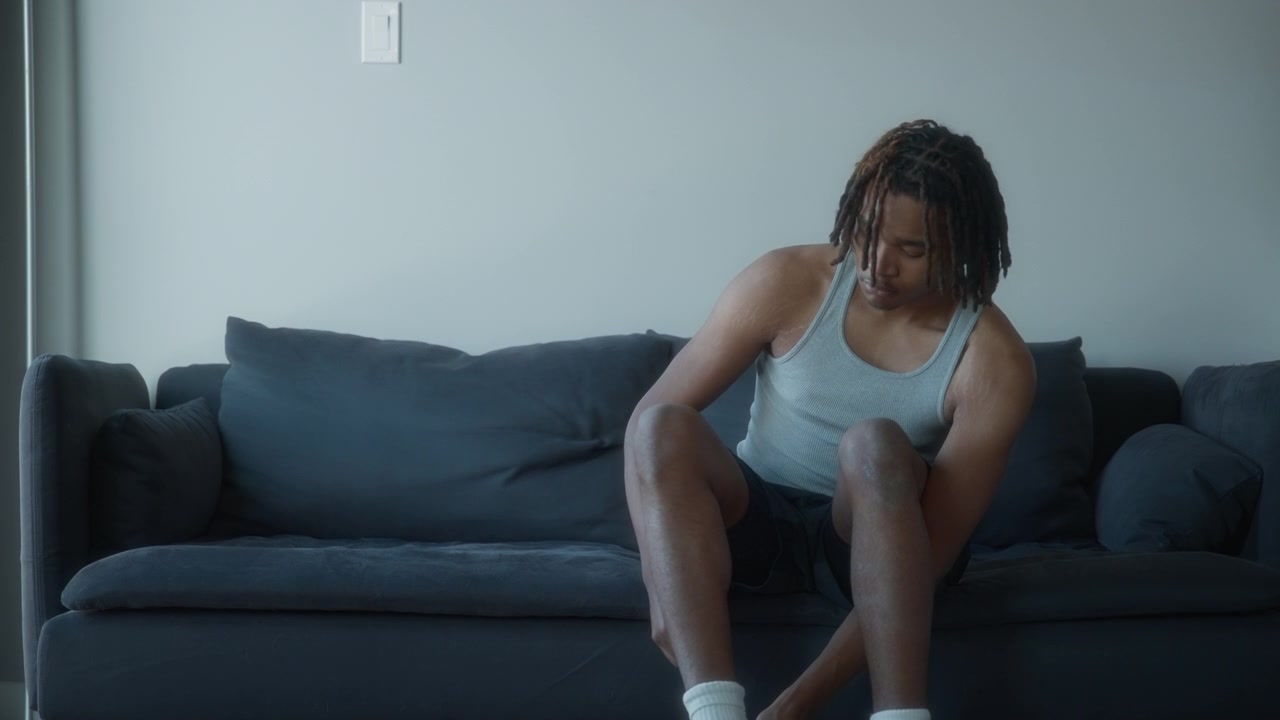 Young man putting his shoes on while sitting on a sofa at home