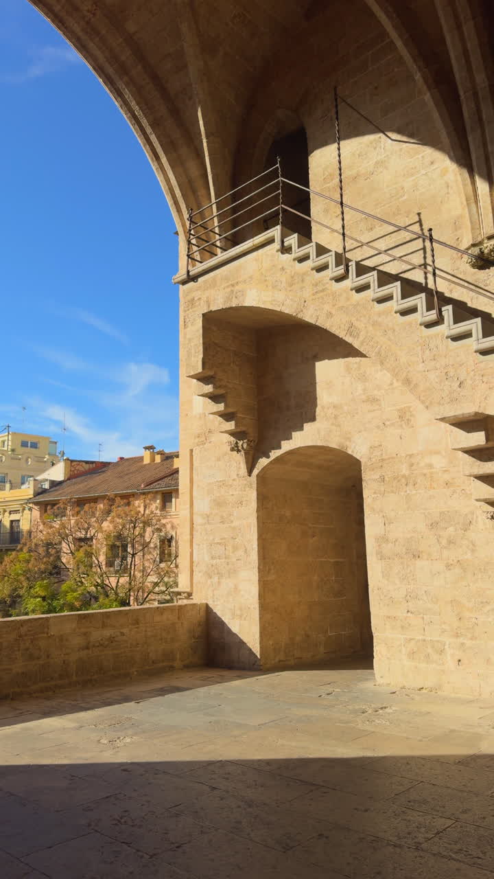 Arco e scale in pietra all'interno delle storiche Torri di Serranos, che rivelano una prospettiva degli edifici della città di Valencia e del cielo sereno