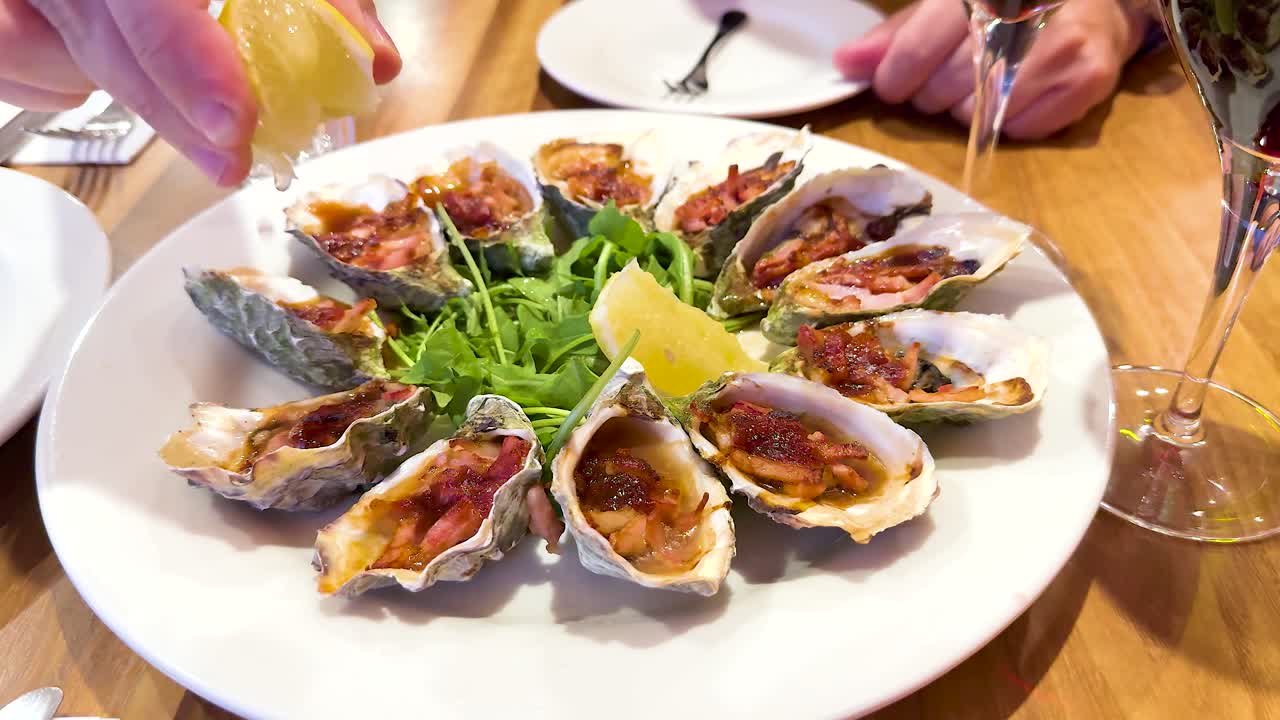 A hand squeezes lemon over a plate of oysters, enhancing their flavor. Bright lighting and elegant presentation create a fresh, vibrant mood