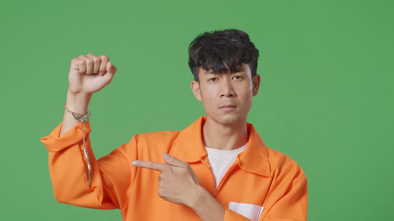 녹색 스크린 배경에 서 있는 아시아 남성 수감자의 클로즈업, 부러진 수갑을 보여주고 그들을 가리키고