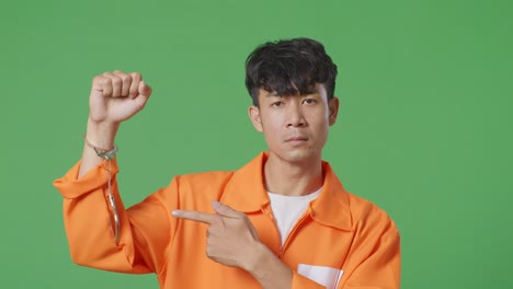 녹색 스크린 배경에 서 있는 아시아 남성 수감자의 클로즈업, 부러진 수갑을 보여주고 그들을 가리키고