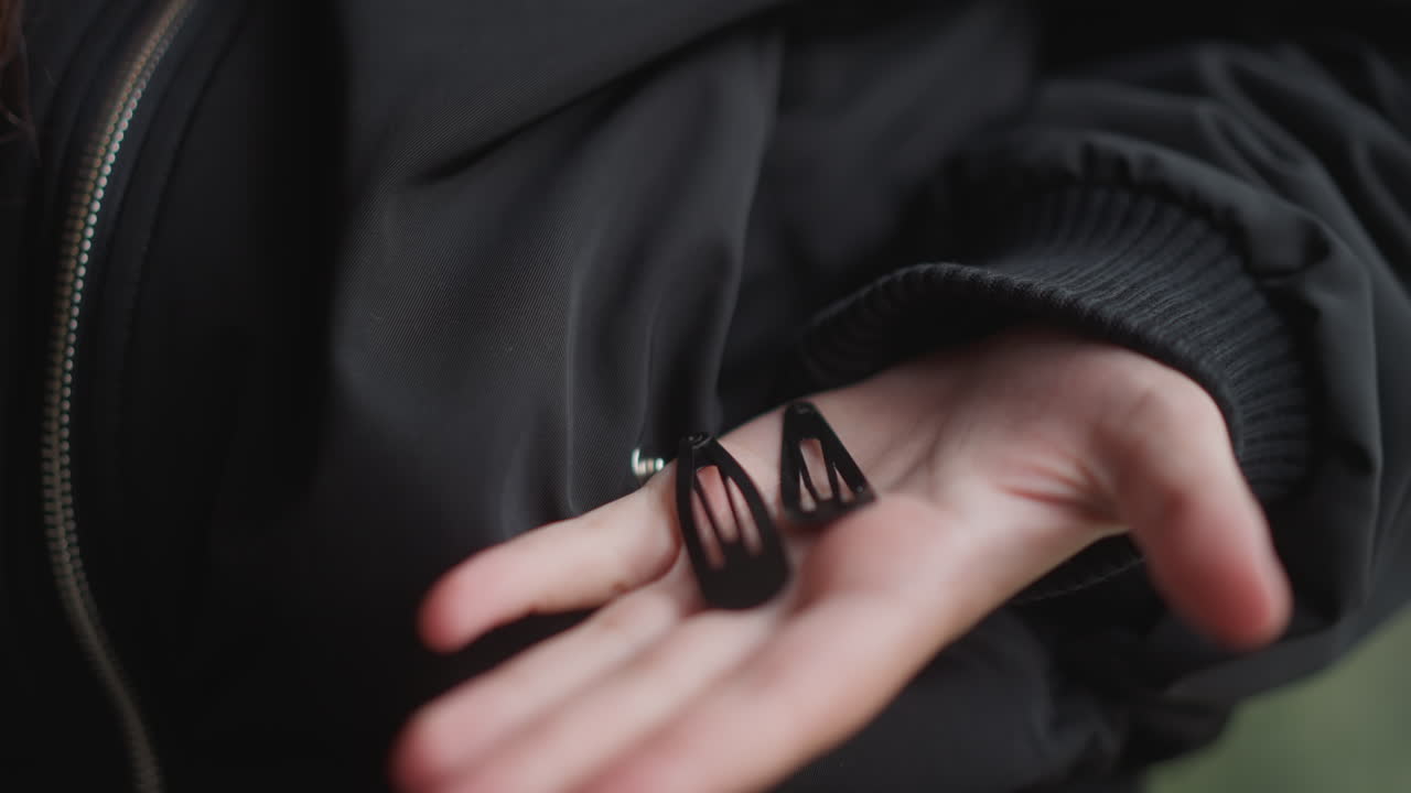 Closeup of woman sharing scrunchies outdoors. Damp jacket and rainy scene with woman offering accessories. Outdoor shot of woman with open hand sharing scrunchies against green rainy background