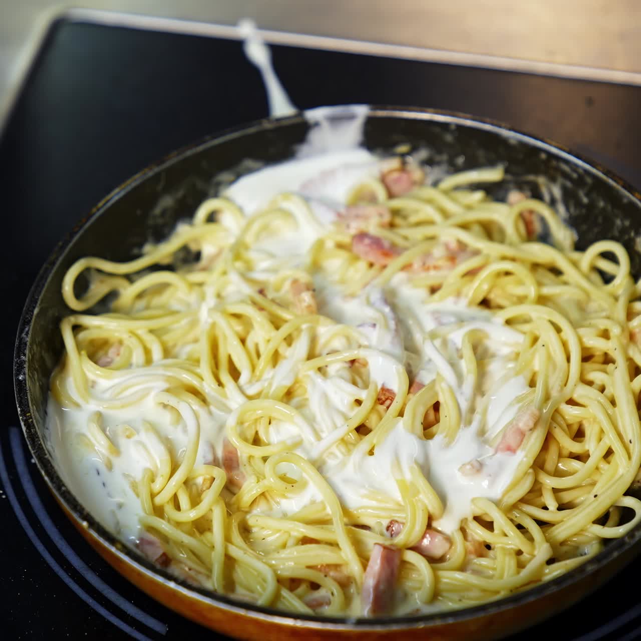 Preparation of a delicious dish in frying pan. Cooking and stirring the spaghetti with white sauce in the frying pan. Close-up