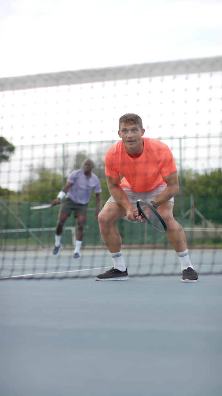 Vertical video of diverse male tennis players playing tennis in slow motion