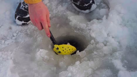 hombre sacando hielo del hoyo de pesca en el lago congelado con una pala de skimmer de hielo