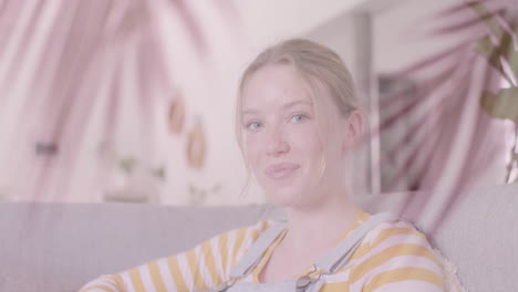 animation of palm leaves over smiling caucasian teenage girl relaxing at home