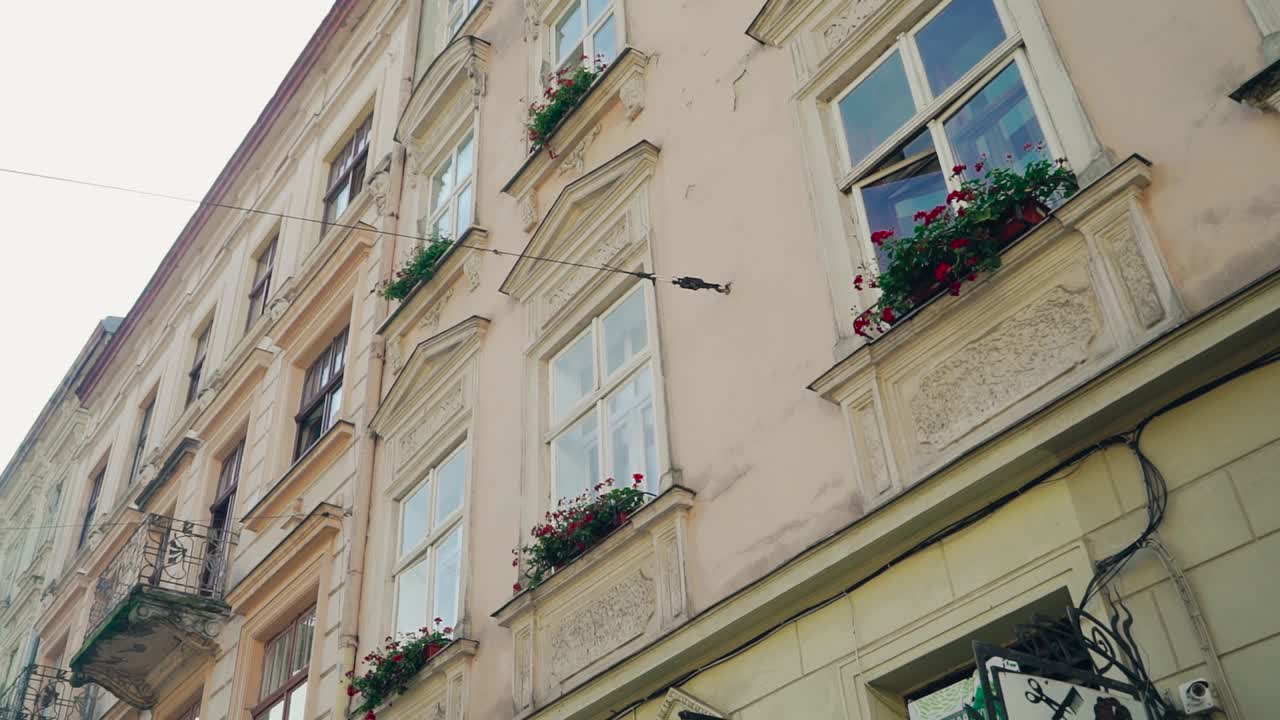 Architectural buildings with flowers on windows in the european city Lviv. Wonderful cityscape of ancient town at day. Motion camera top down.