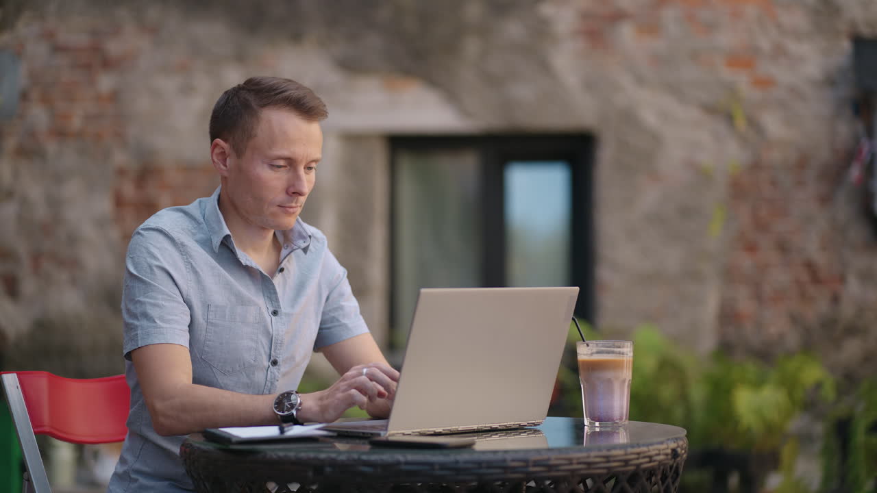 A serious man is a business student working studying sitting at a table and typing a message on a laptop. Typing text on the keyboard