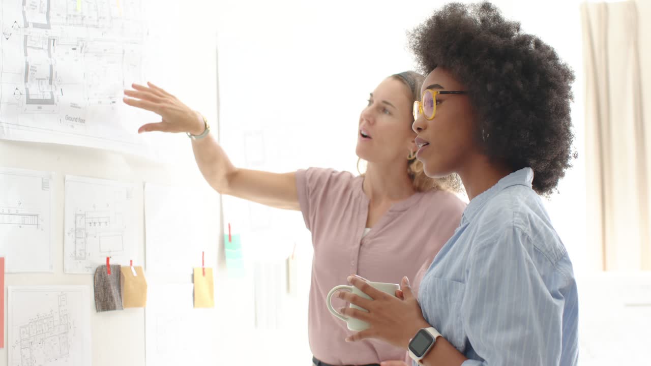 Diverse female team at studio pinboard reviewing plans after tablet tap and pointing, copy space