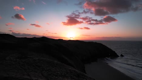 antena: panorámica lenta sobre los acantilados costeros hacia la puesta del sol, bahía de la piscina azul, dron de 4k