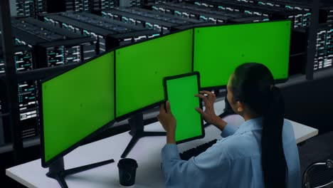 side view of asian woman working with tablet and multiple computer monitor with mock up green screen in data center