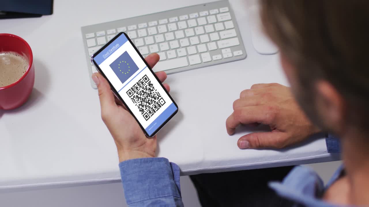 Man at desk holding smartphone with covid vaccination certificate, eu flag and qr code on screen