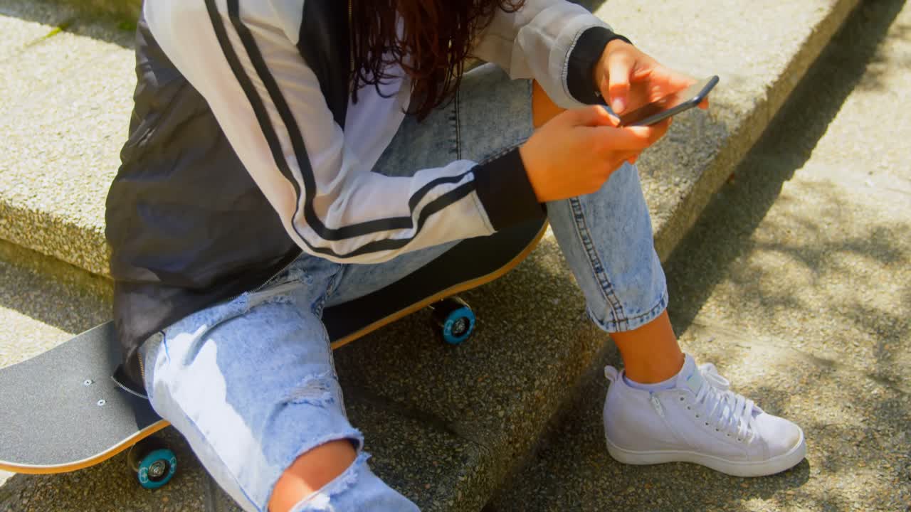 mujer joven sentada en skateboard mientras usa teléfono móvil 4k
