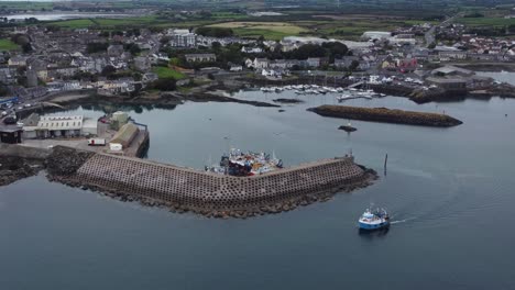 Aerial-view-of-a-fishing-boat-leaving-Ardglass-harbour-on-a-cloudy-day,-County-Down,-Northern-Ireland