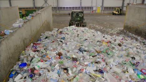 excavadora o cargadora empujando un montón de residuos plásticos en una fábrica de reciclaje