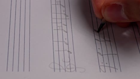 close-up of hand composing second line of music notes with pen on sheet paper
