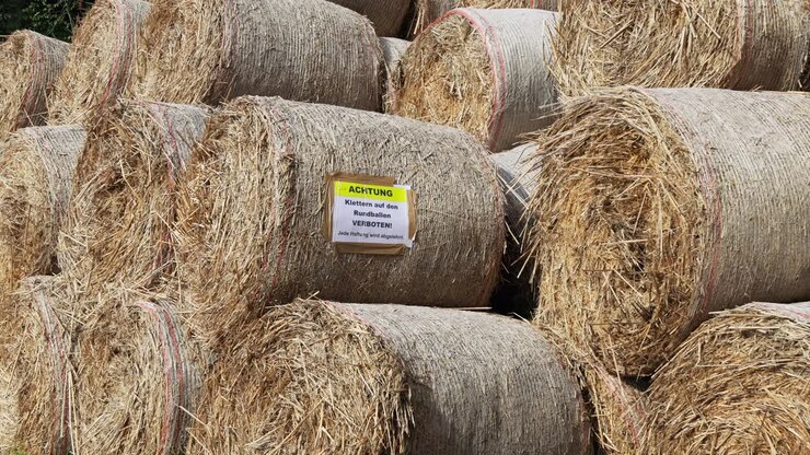 hay bale in close-up with camera panning to the right, german prohibition sign, text translation: attention climbing on the hay bale forbidden, any liability is rejected sign, by day, no persons