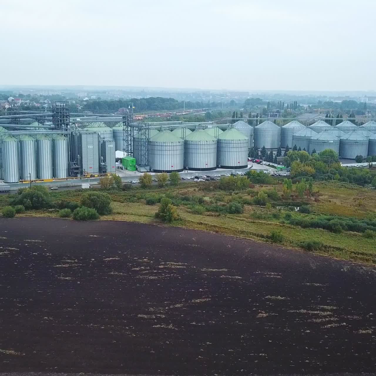 Zahlreiche metallene Aufzugtanks auf dem Gelände einer modernen Getreideanlage. Drohnenaufnahme, die sich von einem riesigen Industriegebiet auf den Feldern entfernt.