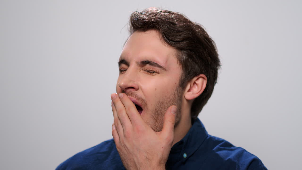 Sleepy man yawning in studio. Tired guy posing on light background