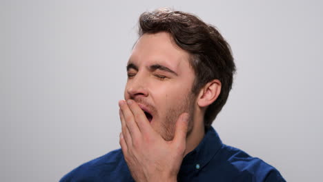 sleepy man yawning in studio. tired guy posing on light background