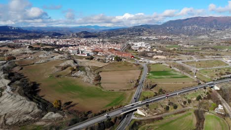 aerial: main road and cars entering a medium-sized town in catalonia with the pyrenees mountain range in the background