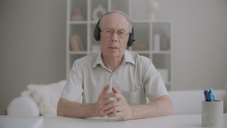 elderly male teacher with headphones is speaking during online education by internet medium portrait of aged speaker