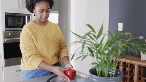 happy african american woman rinsing vegetables in kitchen sink, slow motion