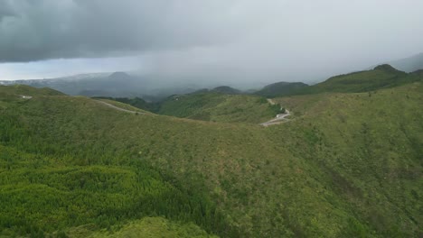 üppige-Grüne-Hügel-Unter-Einem-Wolkigen-Himmel-Mit-Einer-Entfernten-Straße,-Die-Sich-Durch-Die-Landschaft-Schlängelt