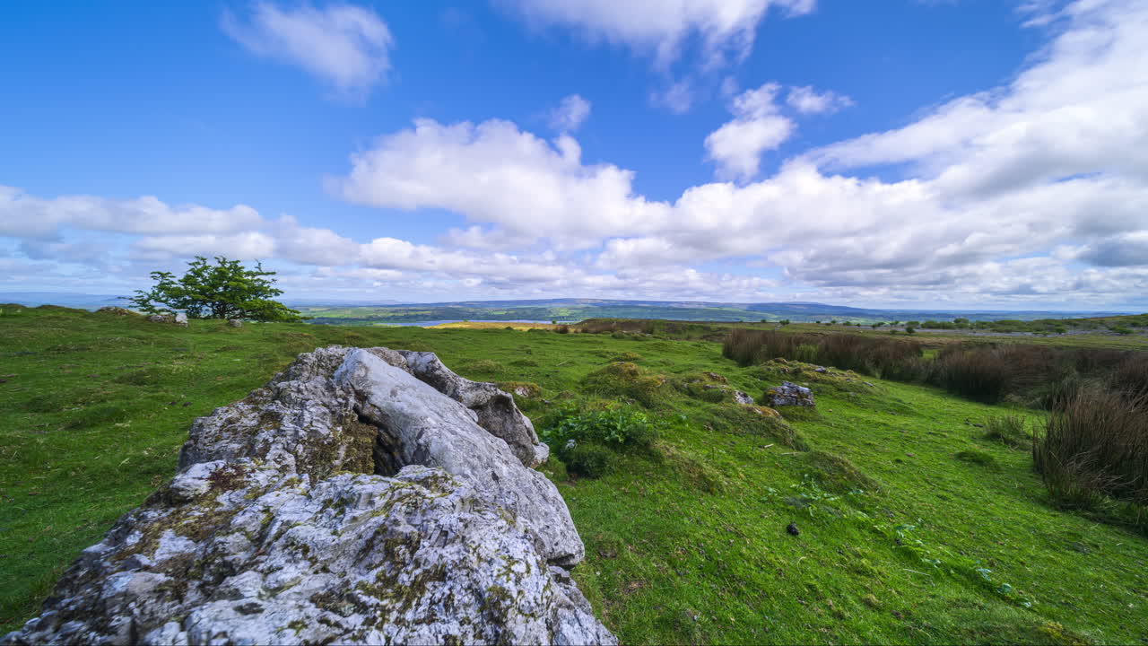 Timelapse af et landligt landskab med klippeformationer og træer i forgrunden samt bakker i det fjerne på en solrig dag med skyer. Set fra Carrowkeel i County Sligo, Irland.
